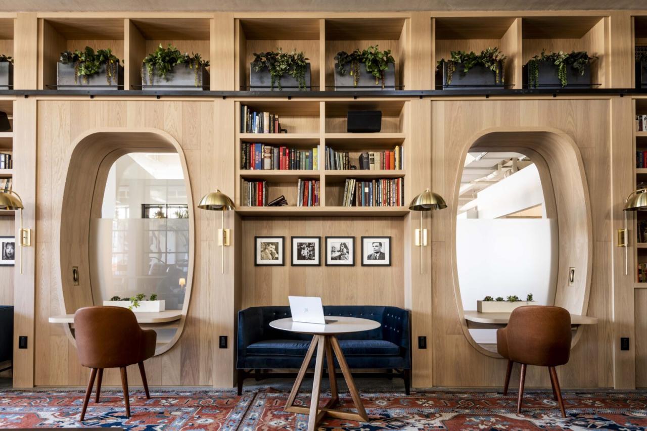 An interior design featuring warm wood tones, green plants in overhead cubbies, and a central seating area with a laptop.