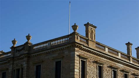 A historic light-colored stone building with patterned stonework and a flagpole under a clear blue sky.