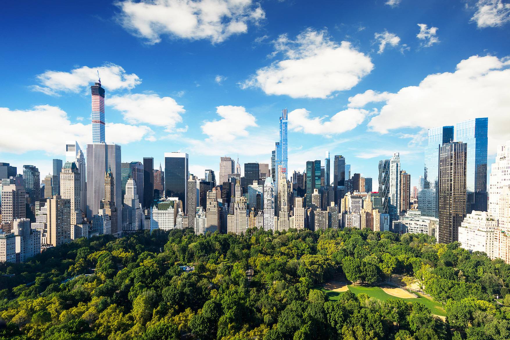 A panoramic view of skyscrapers surrounding a large, dense green park, showcasing urban development alongside nature.