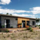 Contemporary modular home with a dark facade and wooden entrance in a rural setting.