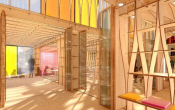A brightly lit, open-plan interior with wooden structural elements, translucent partitions, and colorful accents, including yellow, orange, and red panels.