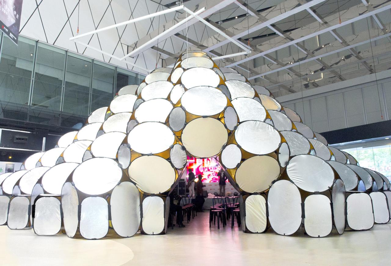 A unique, dome-shaped structure made of overlapping, light-colored circular and oval panels, creating an interesting geometric pattern in a large indoor space.