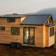 A portable tiny house with a rustic wooden exterior and a dark metal roof.