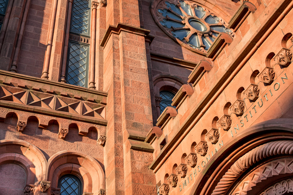 Close-up of a red brick Gothic Revival building facade with intricate stone carvings and a large rose window.