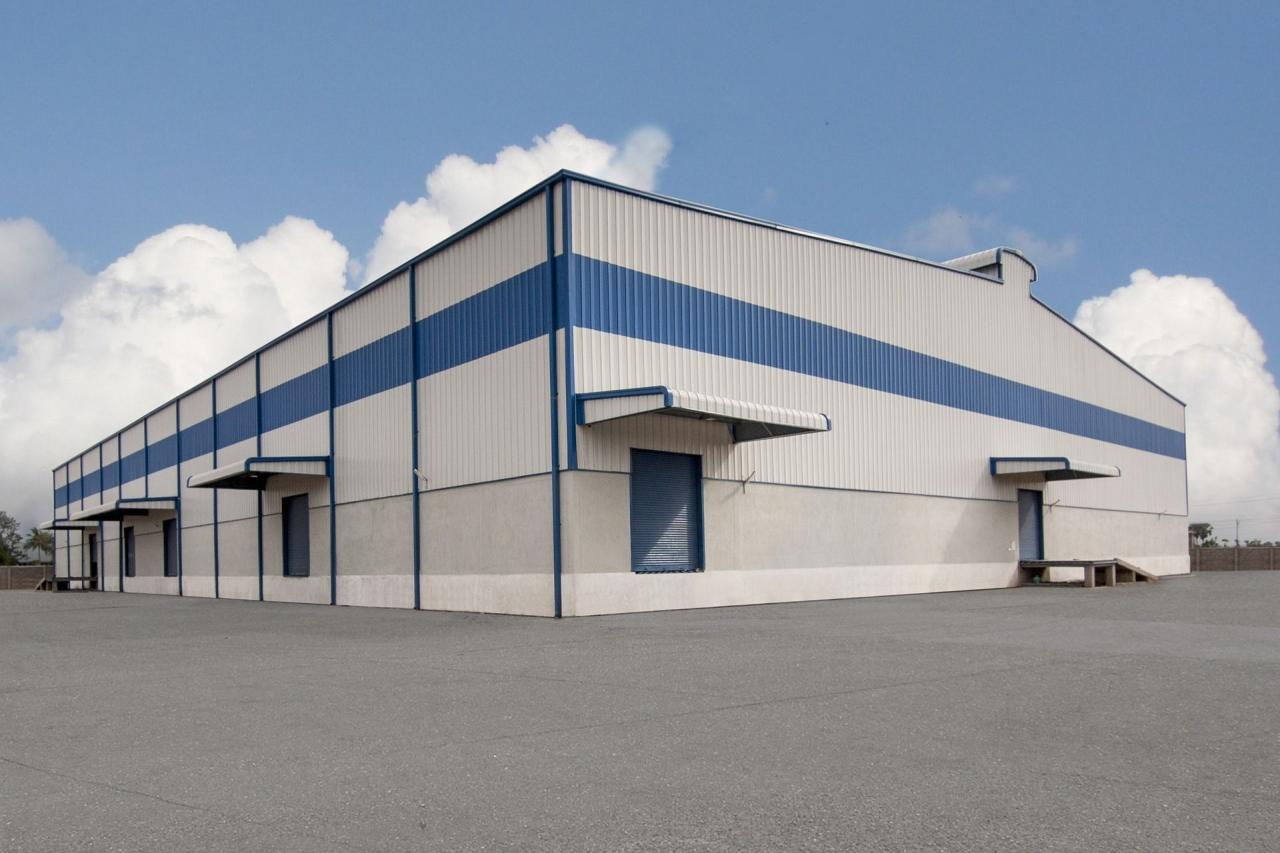 A commercial building with a pre-engineered look, featuring roll-up doors and awnings under a partly cloudy sky.